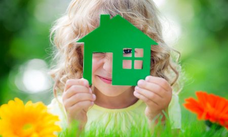 Happy child holding house in hands against spring green background.