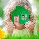 Happy child holding house in hands against spring green background.
