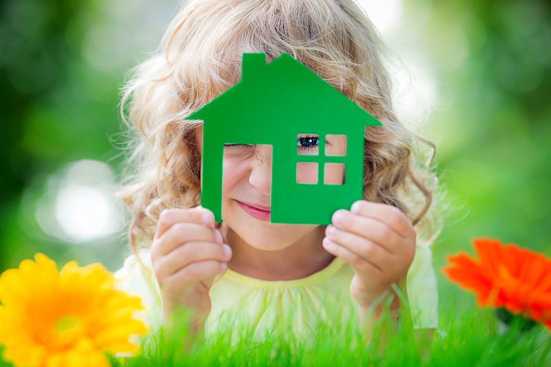 Happy child holding house in hands against spring green background.